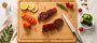 Nolly Home Premium Large Bamboo cutting board with sliced meat, vegetables, and a knife on a light surface.